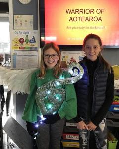 Two students presenting their light suit. The students are standing in front of a projected slide which reads, “Warrior of Aotearoa”.  