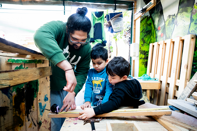 A kaiako is working together with two children to create something out of wood.