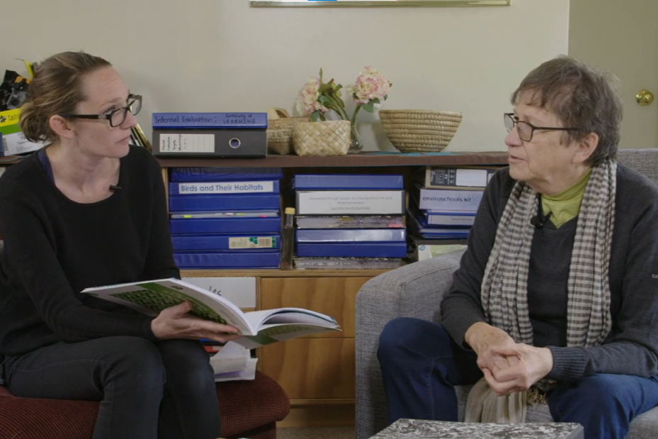 Two kaiako are having a discussion over a copy of Te Whāriki.