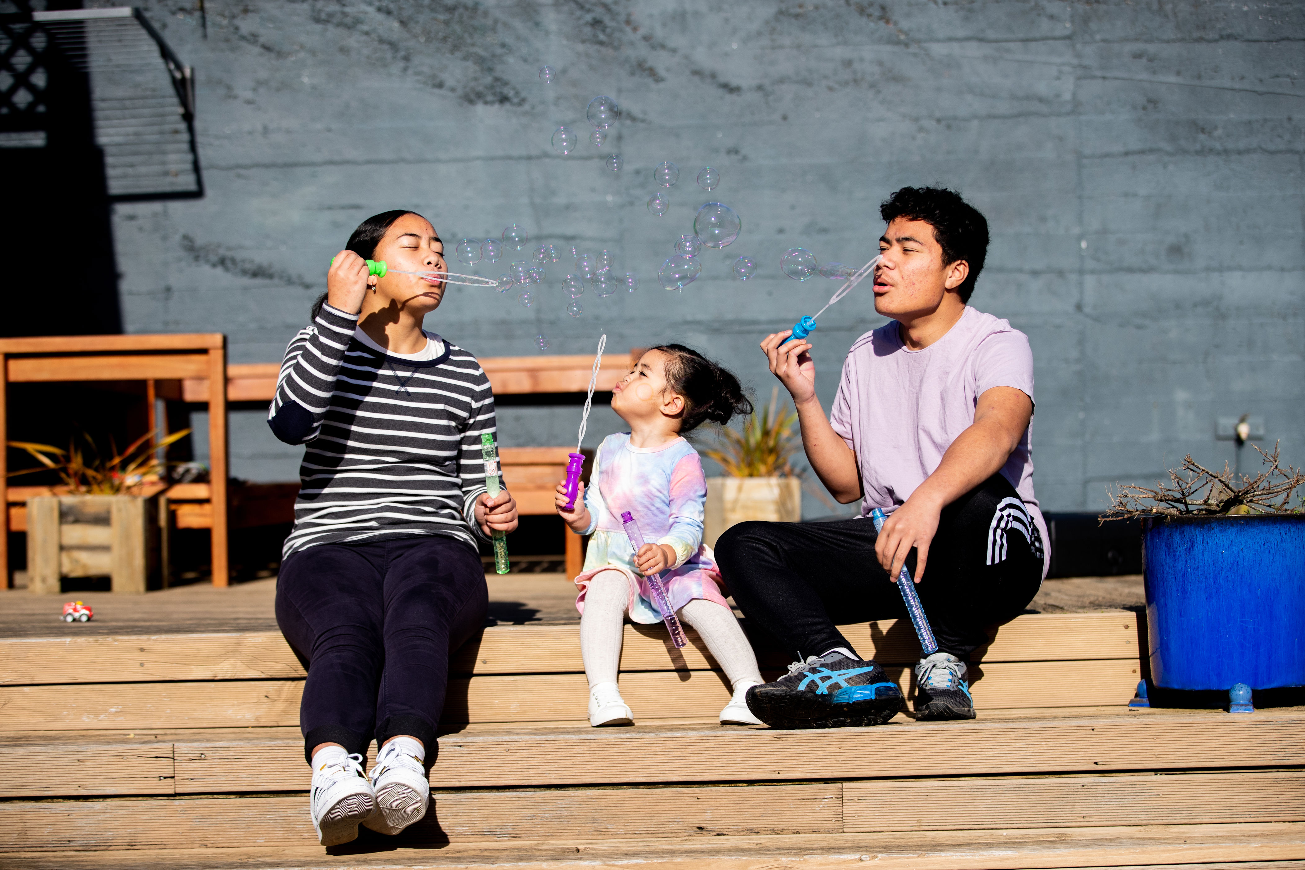 Two adults and a child blowing bubbles together outside.