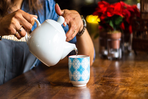 A close up of someone pouring tea from a teapot into cup.