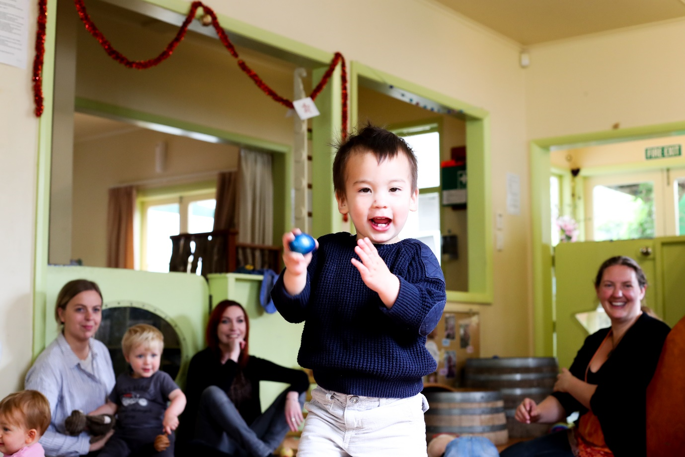 A child is playing with a small ball surrounded by children and kaiako.