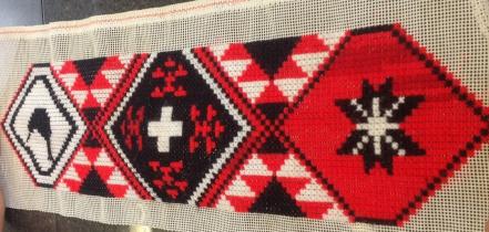 A red, black and white tāniko on display on the classroom wall.