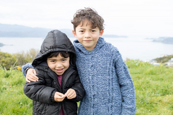 Two tamariki of different ages giving each other a hug while exploring the outdoors