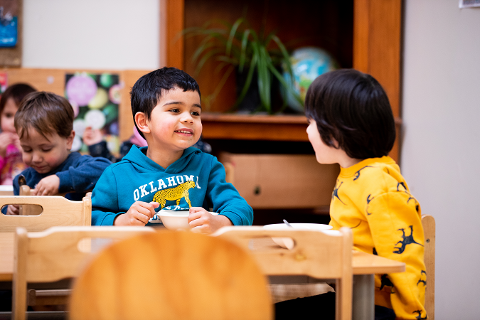 A child sitting and smiling at the kai table with another child