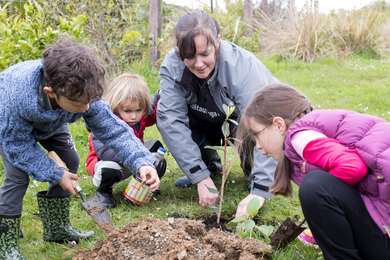 A group of children and a kaiako planting a tree together