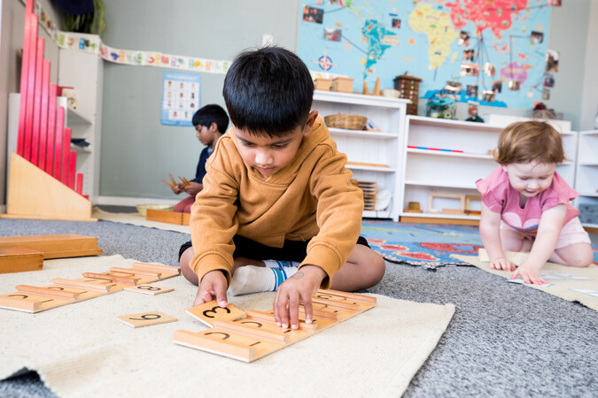 A young boy in the classroom doing a puzzle on the play mat