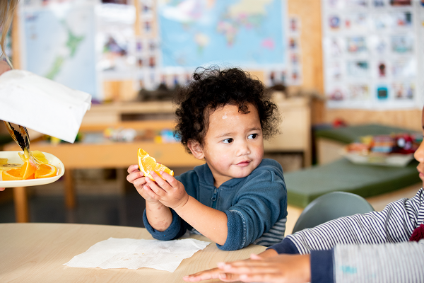 child with a piece of orange sitting at a table