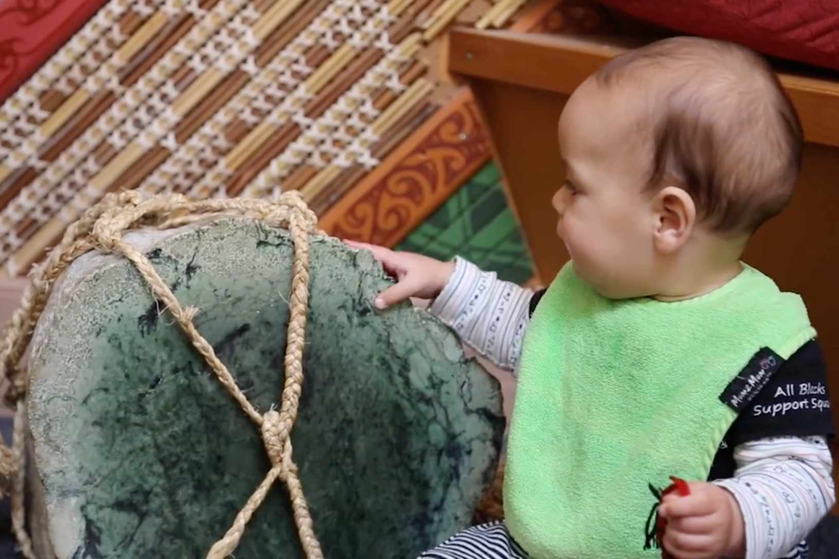 A toddler feels a pounamu stone in the wharerau