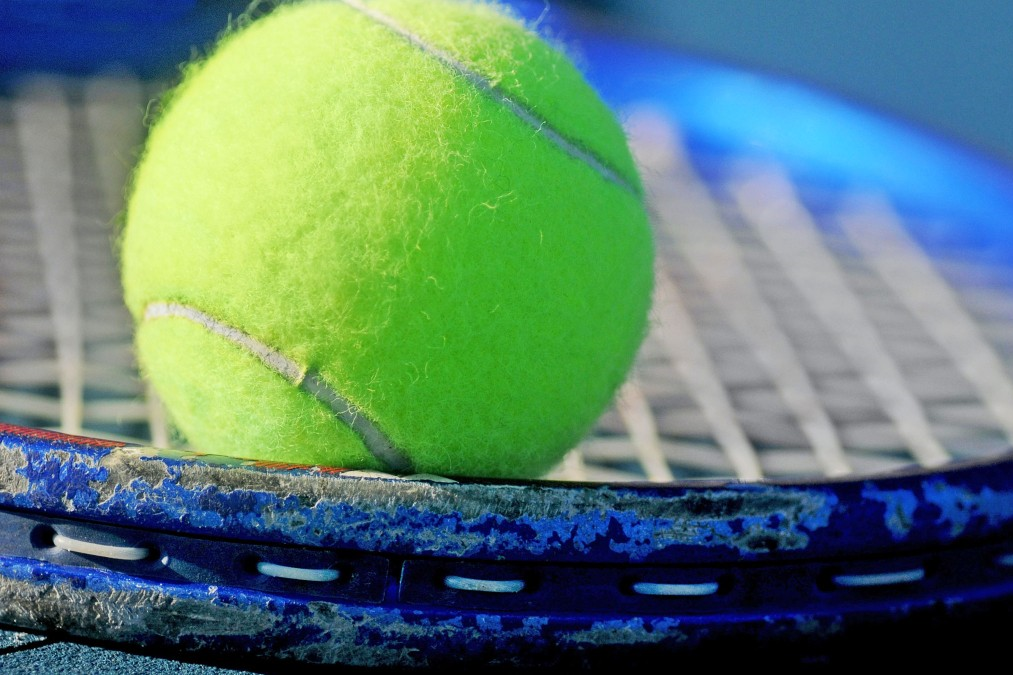 A tennis ball resting on a tennis racquet.