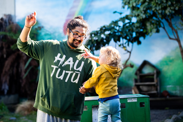 An adult and a toddler outside together point up at the sky.