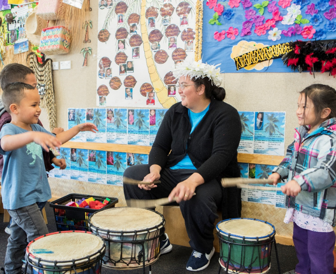 Kaiako playing drums with three children indoors