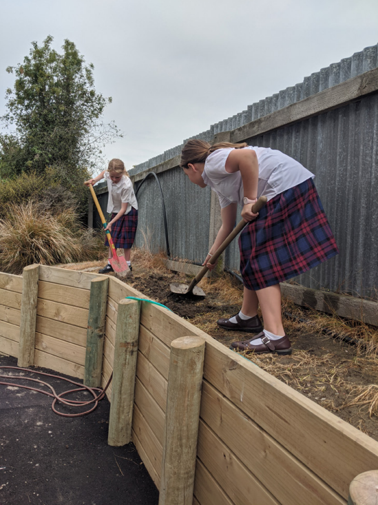 Two students flattening soil in a new raised garden bed.