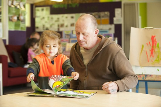 Child turning pages of a book while a kaiako listens to their ideas