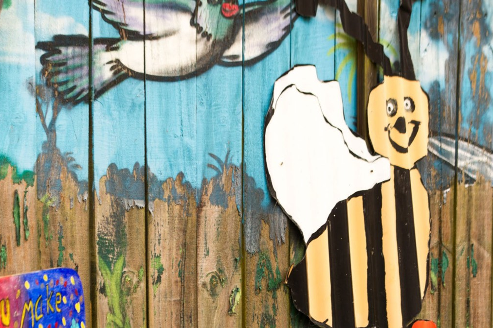 A mural on a fence of a bumble bee and a bird.