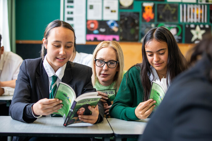 Teacher and students sit together reading books.