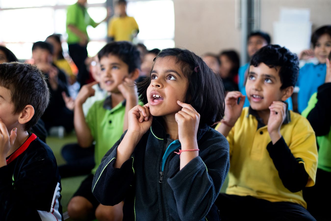 Young children sitting in class with their attention focused forward and hands on cheeks