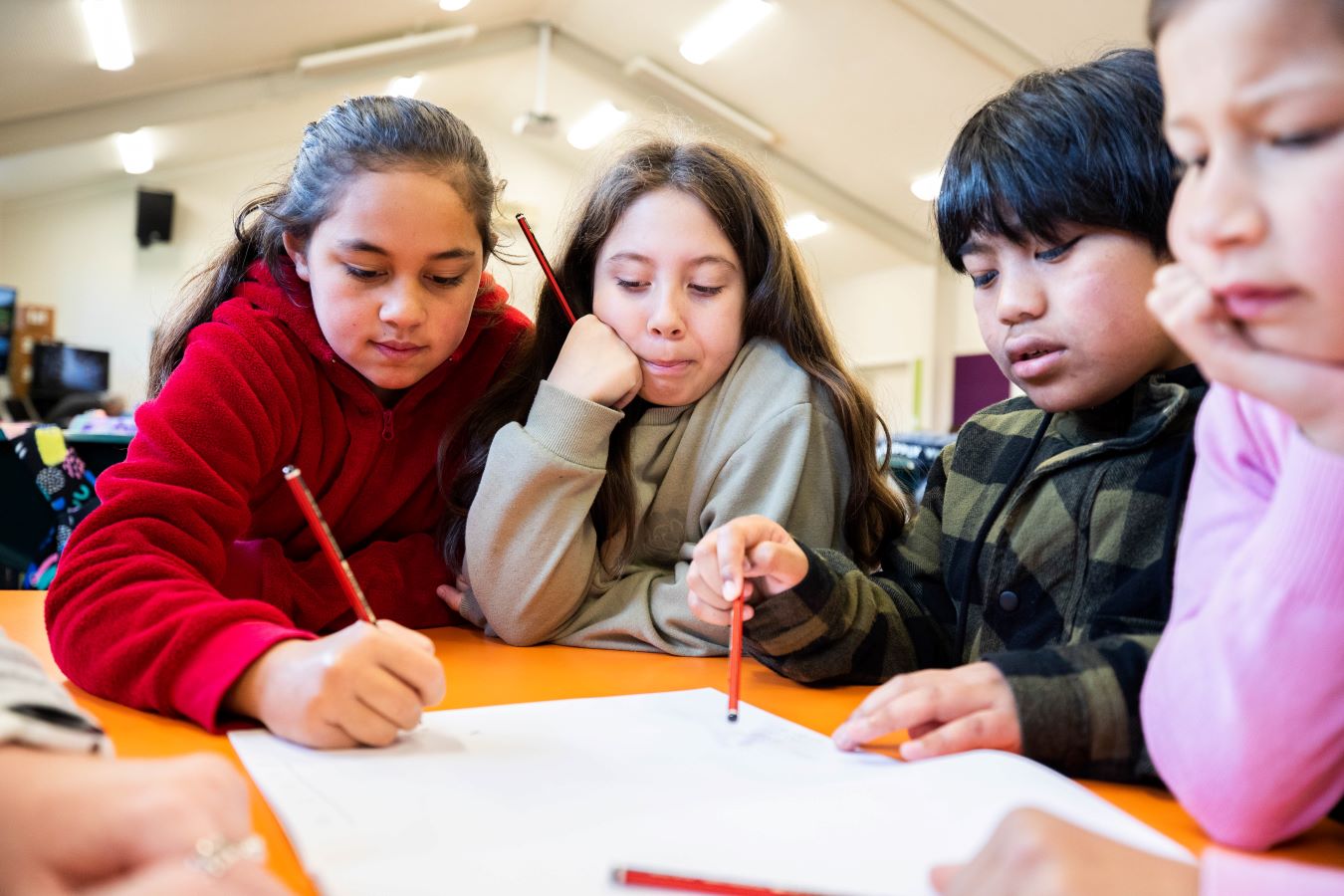 Four children interacting at a table writing and sharing ideas.