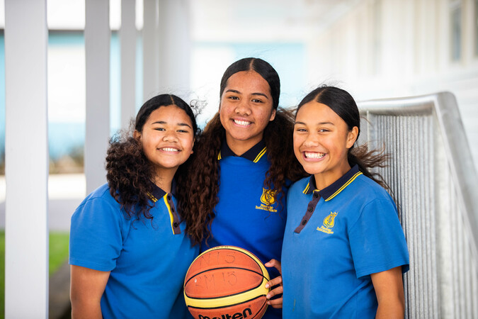 Three girls smile at the camera holding a basketball. 