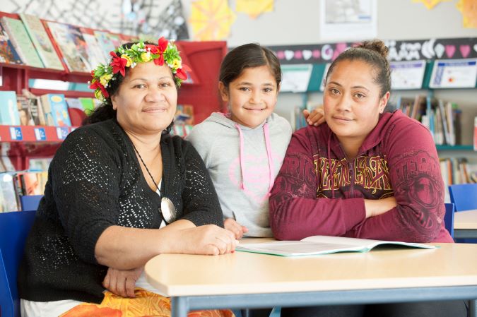 Two polynesian women and young girl at table readingjpg