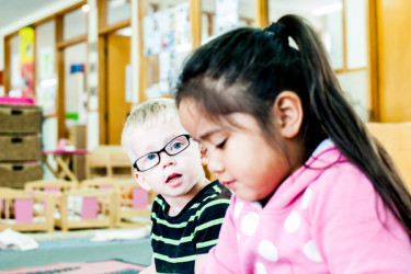 Two tamariki sitting next to each other, one looking up to the other