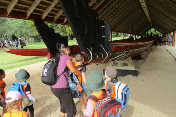 Child being lifted up to to hongi the waka Ngātokimatawhaorua