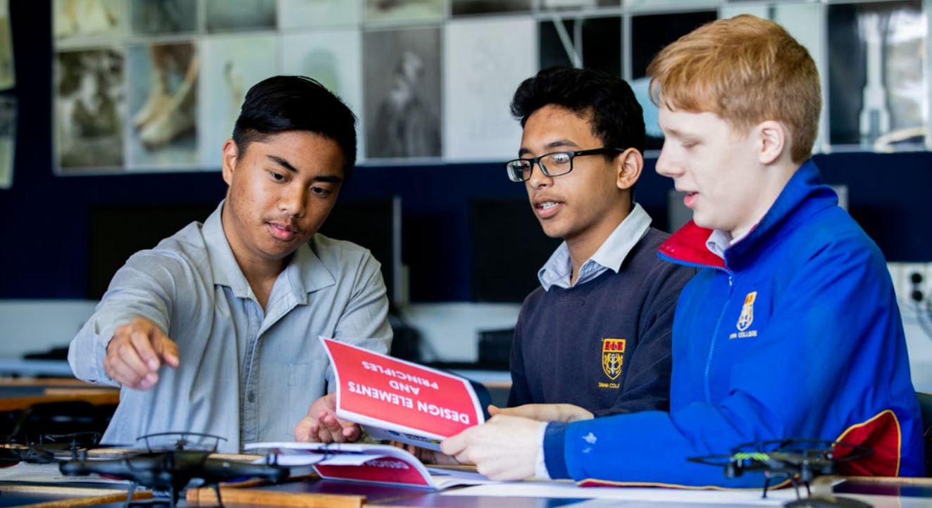 Three students seated at their desks looking at a model plane.jpeg