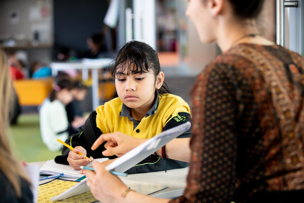 Tamariki sitting with kaiako writing in their notebook.