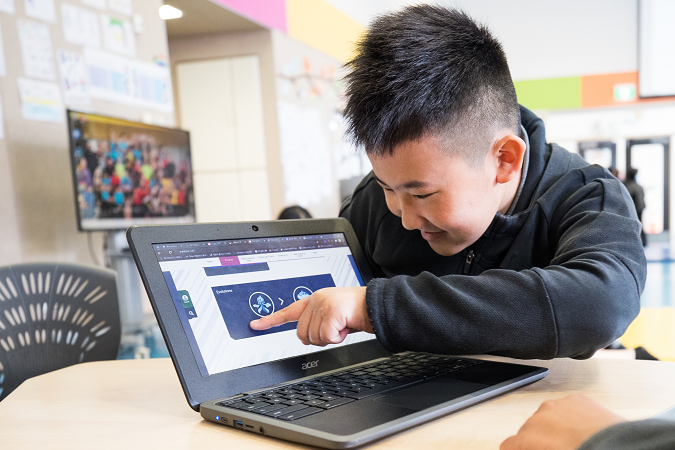 Child pointing to laptop screen and smiling.