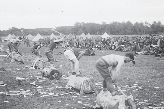 Black and white photograph shows a group of soldiers chopping tree trunks with axes.