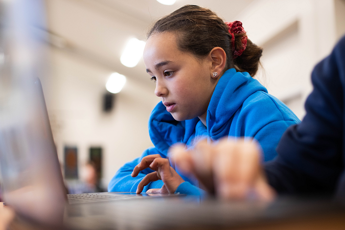 Tamariki sits at the table working on their laptop.