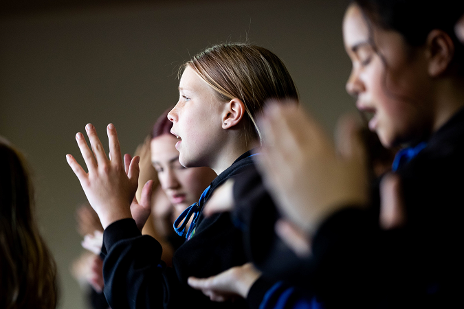 Children standing, clapping hands and singing.