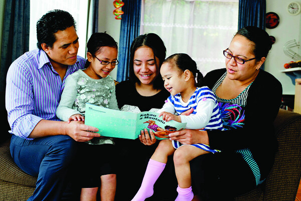 Family of five sit on the couch together reading a picture book.