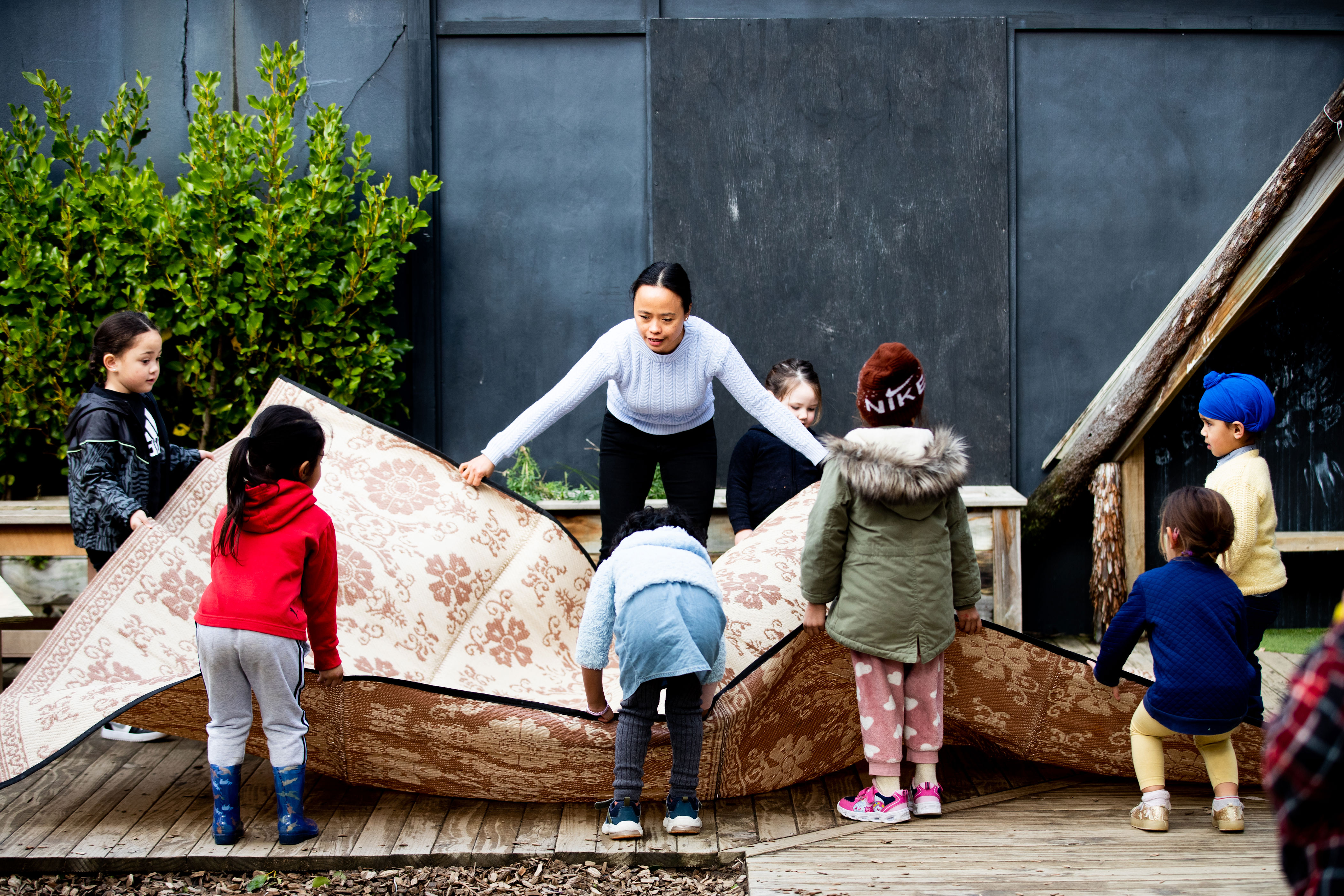 Kaiako and group of children laying out a big whāriki (mat)