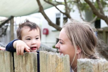 A kaiako engaging with a child who's looking over a fence.