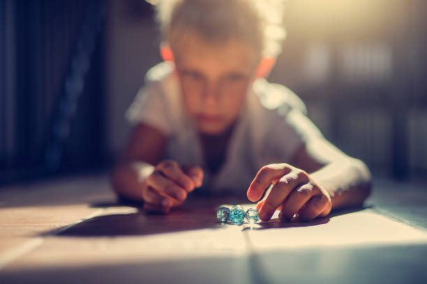 Tamariki lying on the ground as they play a game of marbles. 