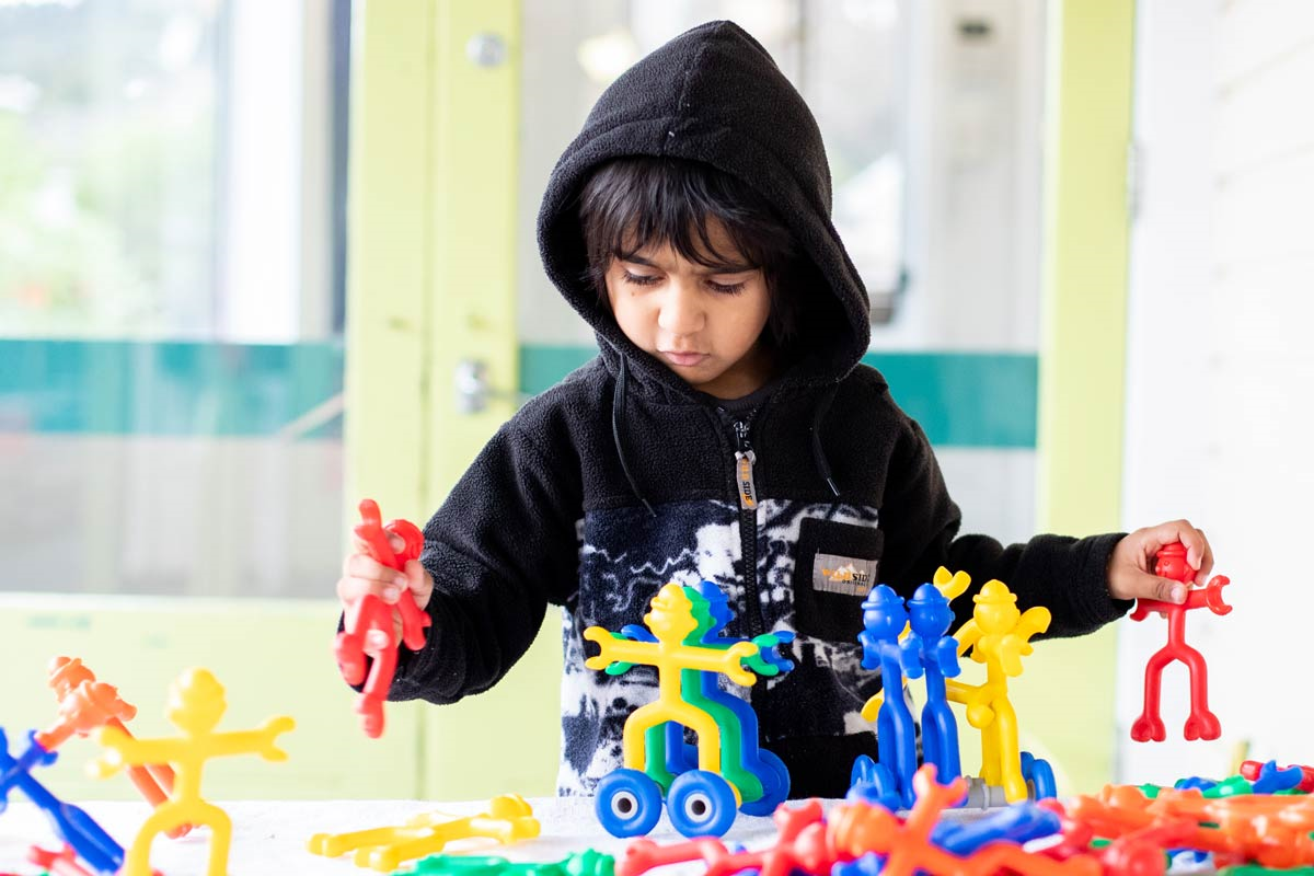 A tamaiti playing with colourful plastic stick figures.