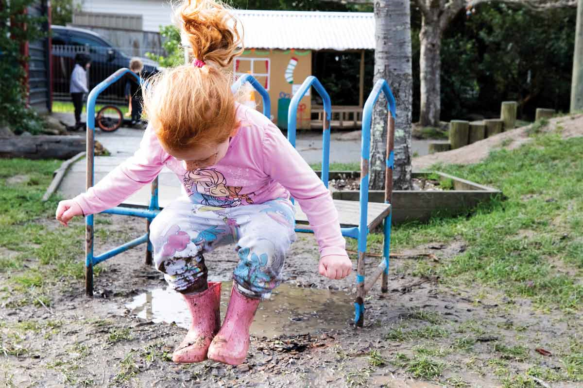 A child is in gumboots jumping in puddle of mud.