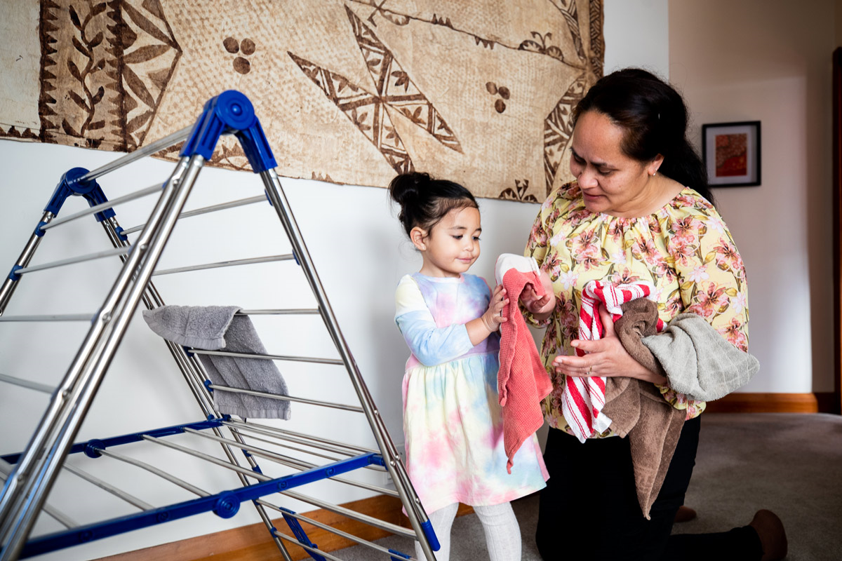 A tamariki helping her tāua hang washing on a clothes rack.