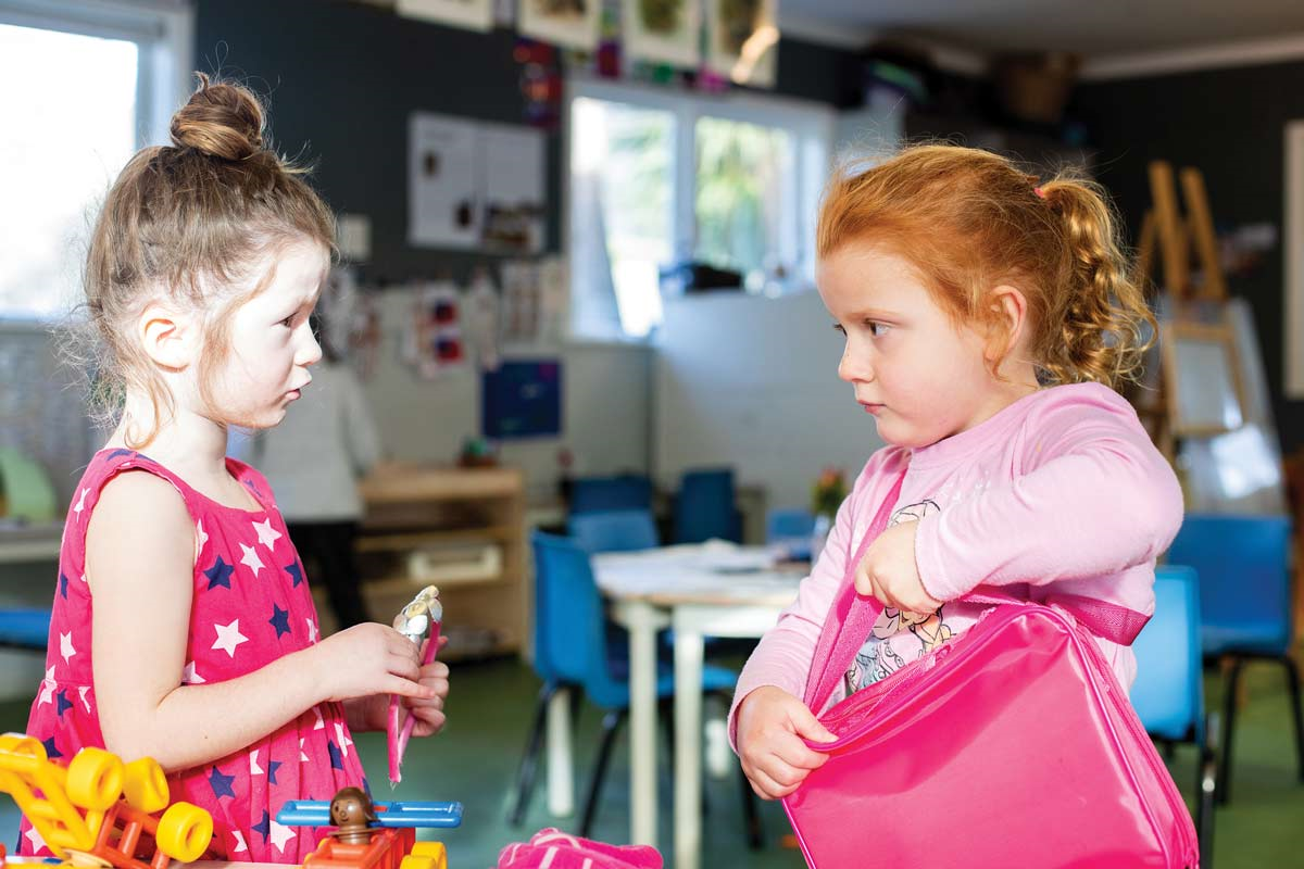 Two children in a classroom talking to each other. 