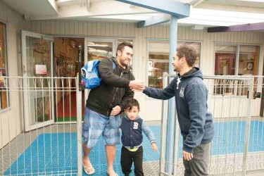 A parents with their child shaking hands with a teacher at the Community Kindy Greenwood gate.