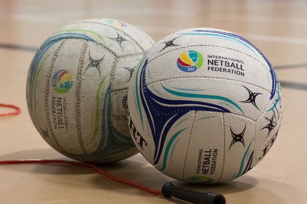 Two netballs and a skipping rope sit on an indoor court.