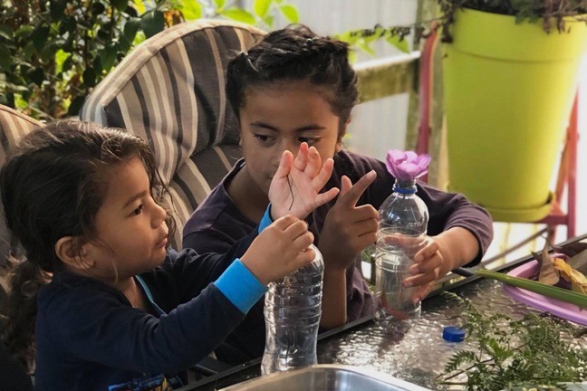 Two children using objects from outside and putting into bottles