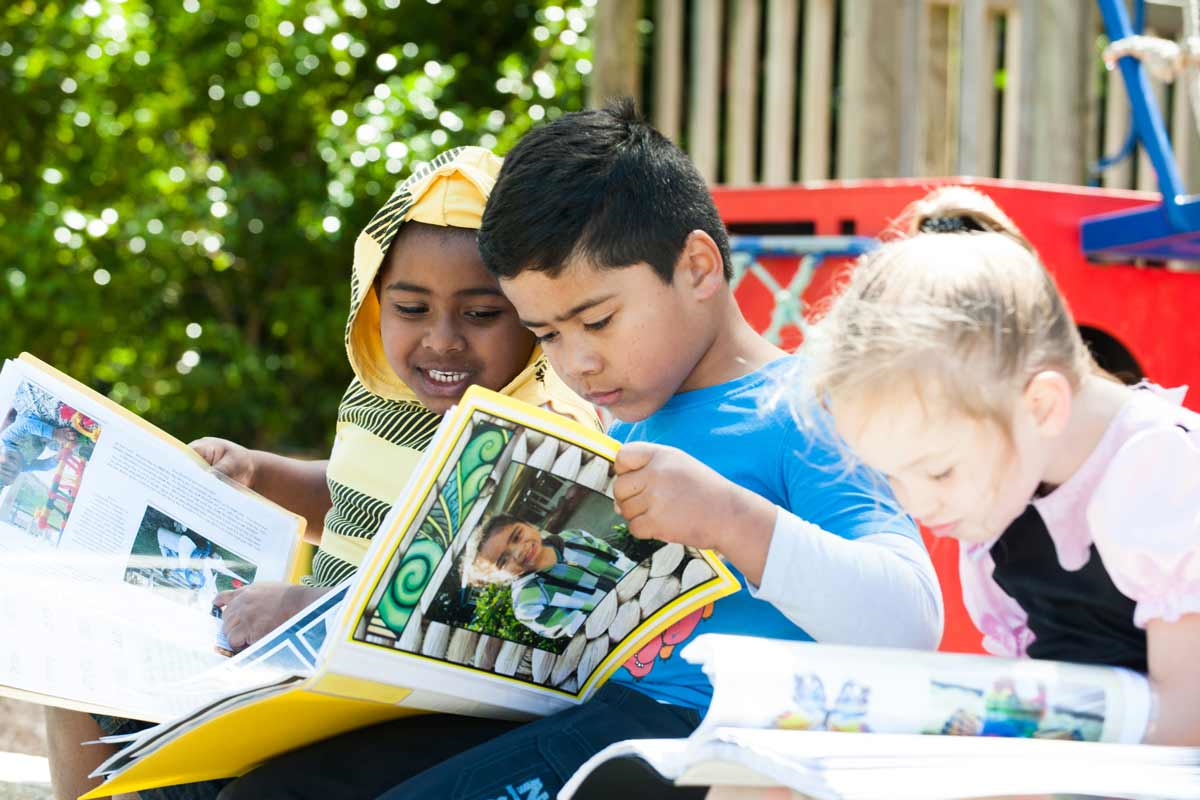 Three children outside reading together.