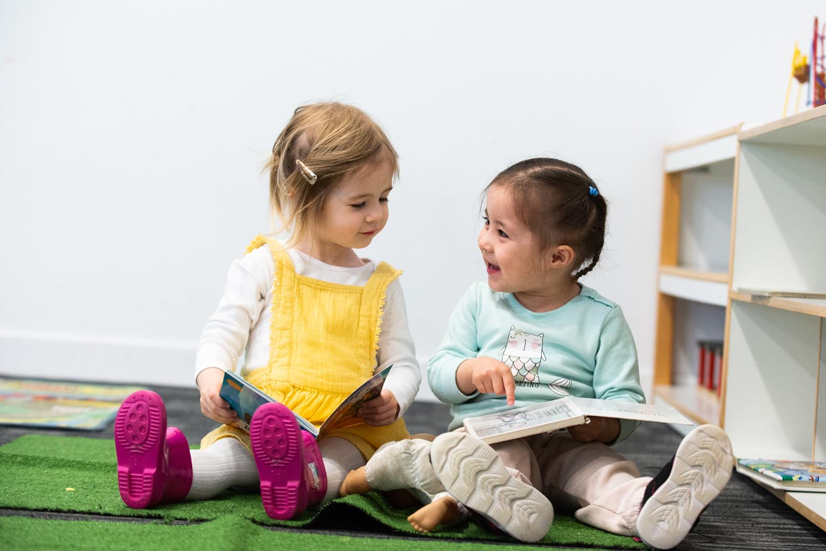 Two tamariki reading together on synthetic grass.