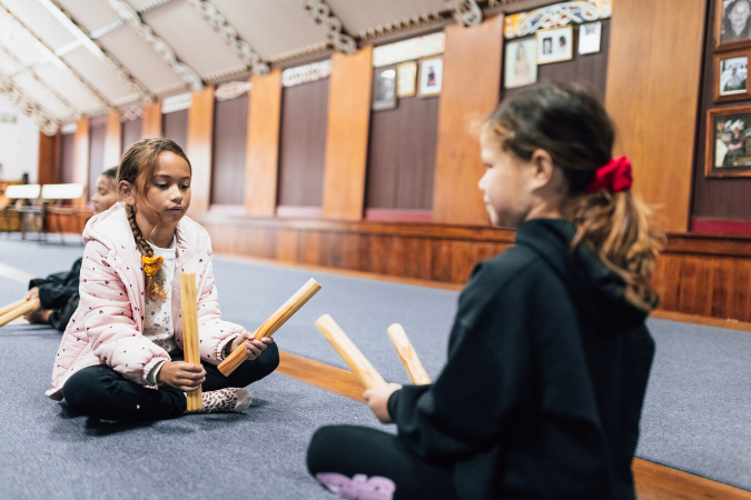 To young girls playing Titi Tōrea (a Māori stick game)