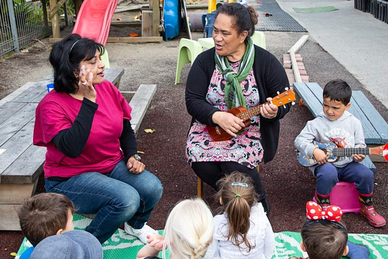 Kaiako sing, sign, and play the waiata Te aroha with a group of children