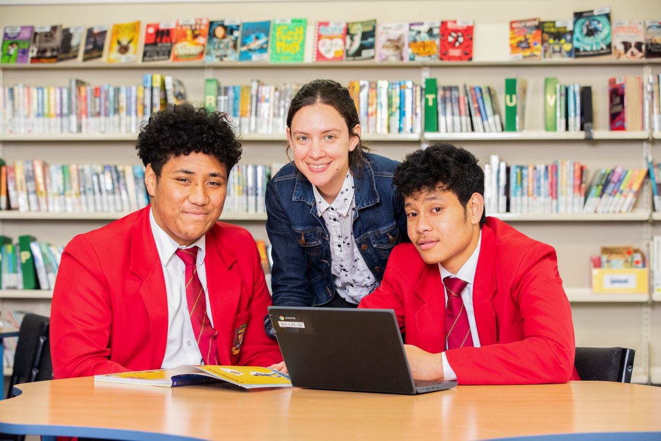 Kaiako and ākonga sit in the school library smiling at the camera. 