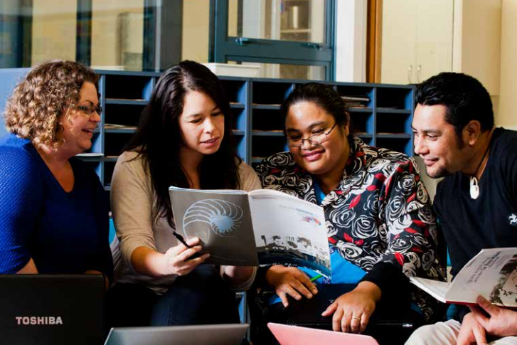 Four kaiako sit together reading a curriculum guide book together.