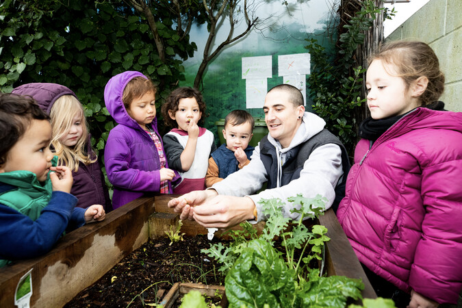 A teacher and children gathered around a raised garden bed.